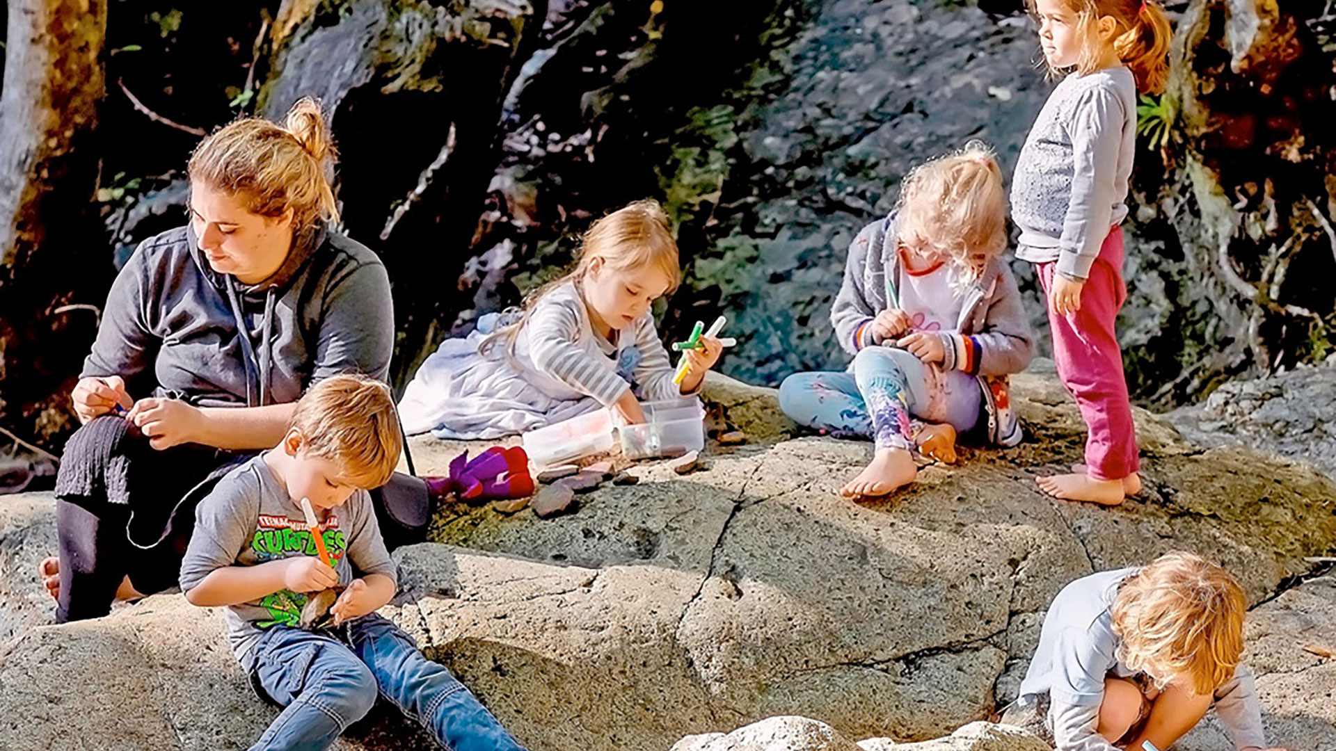 Bambini che disegnano seduti in riva a un ruscello